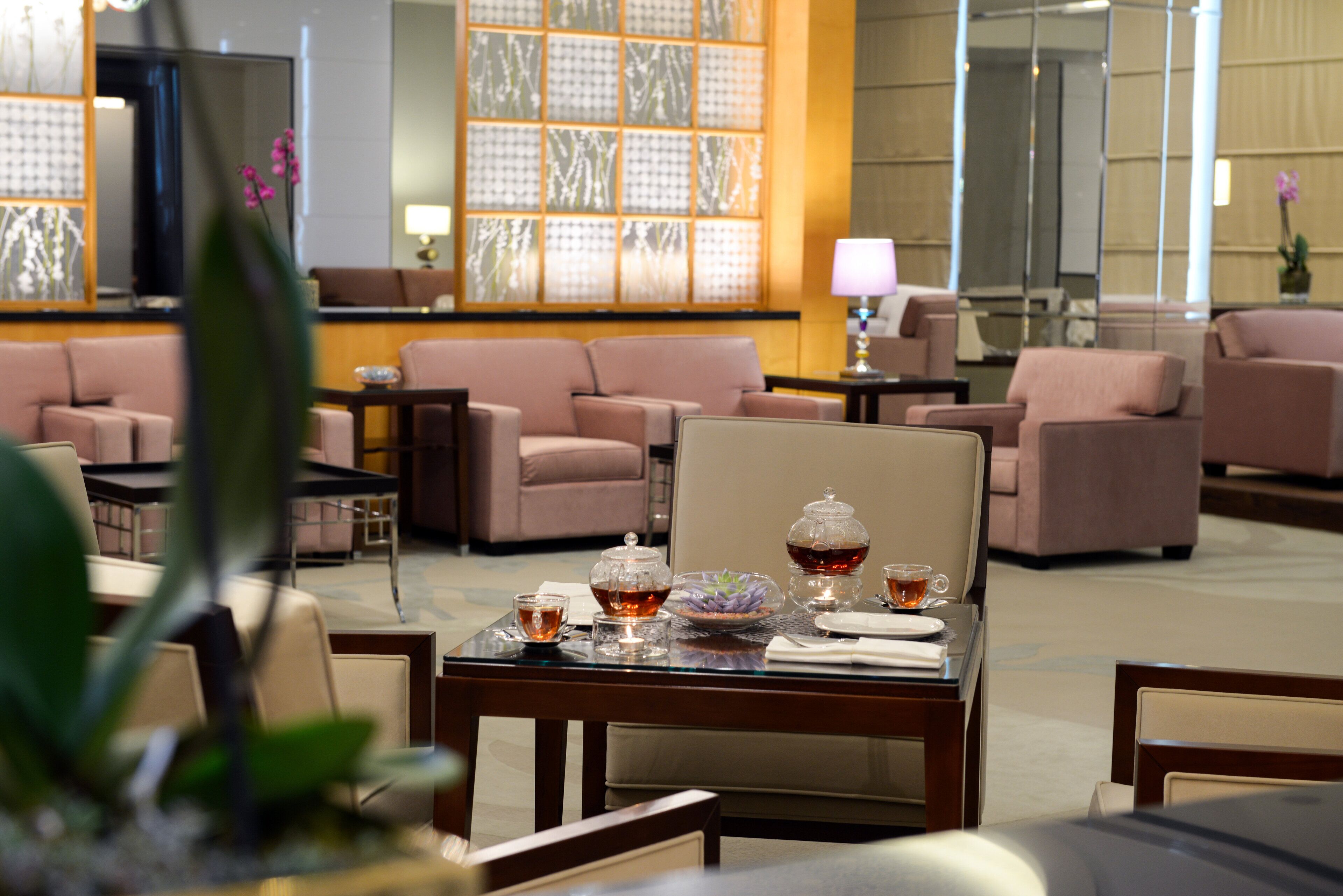 A hotel lobby with sofas, a coffee table with tea service, and a decorative wall.