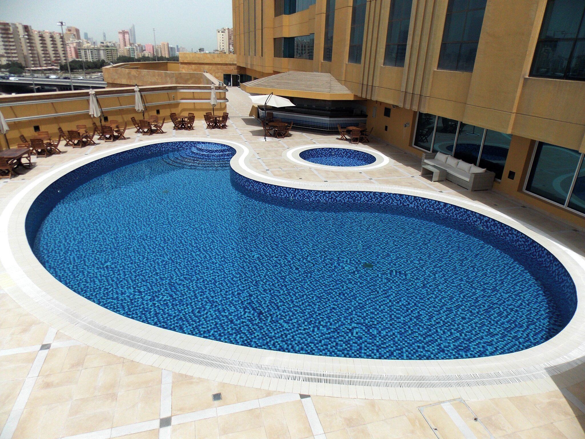 A rooftop swimming pool with a tiled edge, surrounded by lounge chairs and a sunbed.