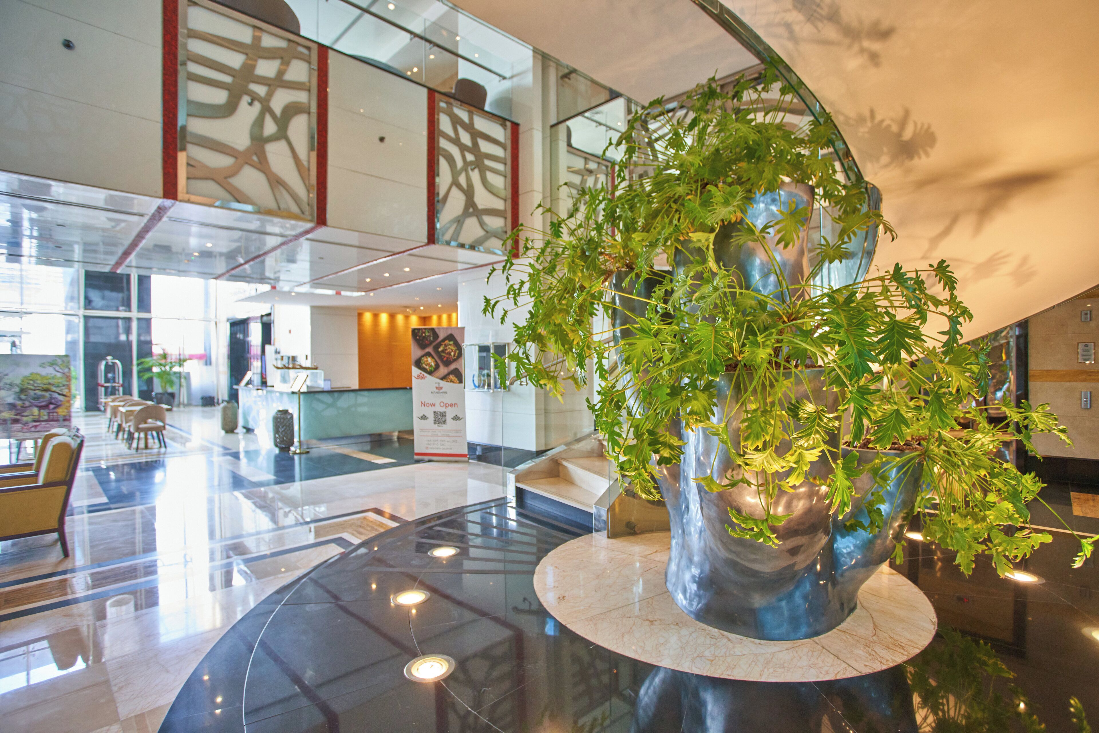 A lobby with a large, modern sculpture of a tree in a metallic bowl, a reception desk, and a seating area with chairs.