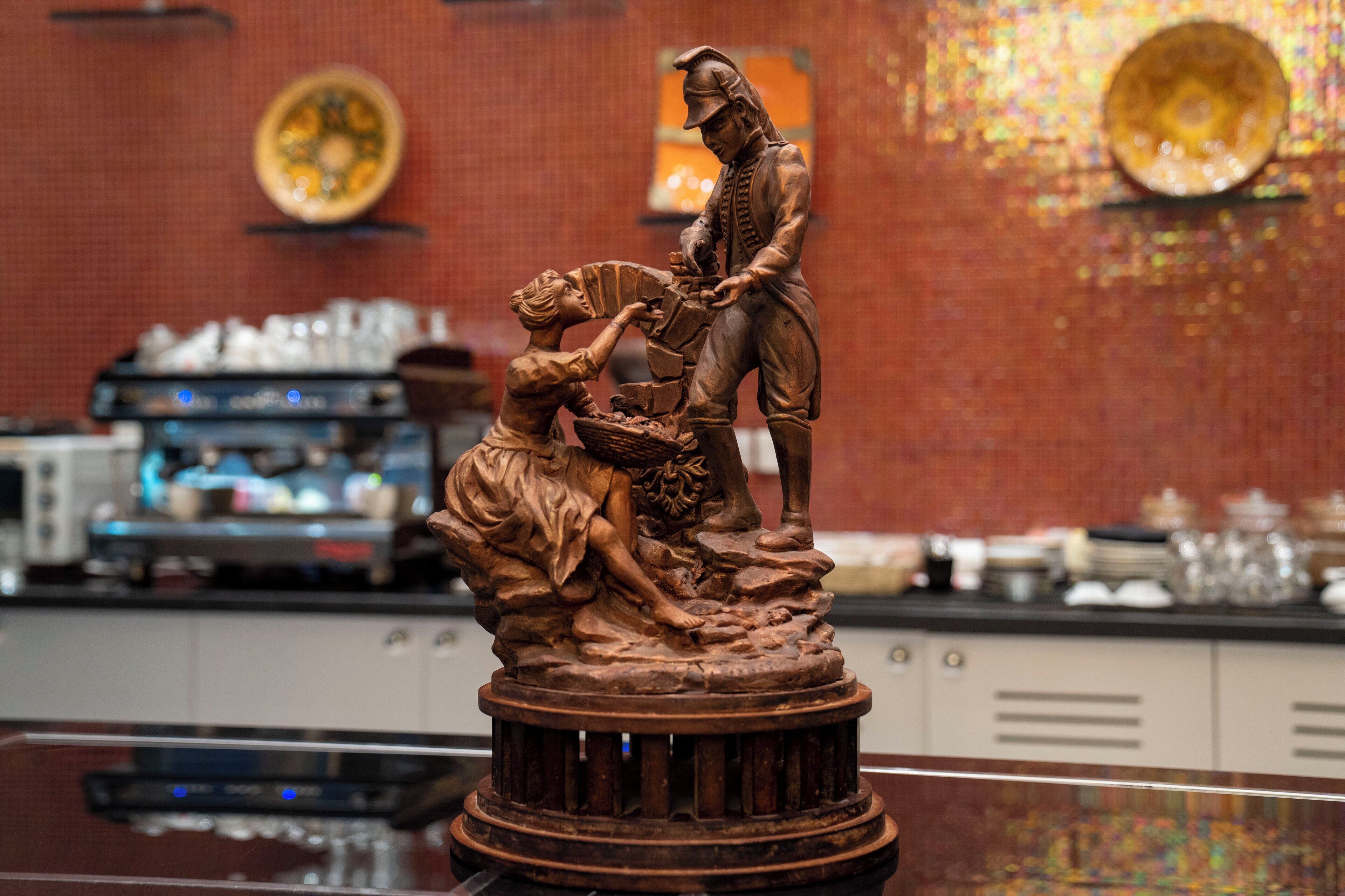 Una estatua de bronce de un hombre y una figura arrodillada sobre un pedestal, en un ambiente de restaurante.