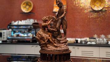 Una estatua de bronce de un hombre y una figura arrodillada sobre un pedestal, en un ambiente de restaurante.