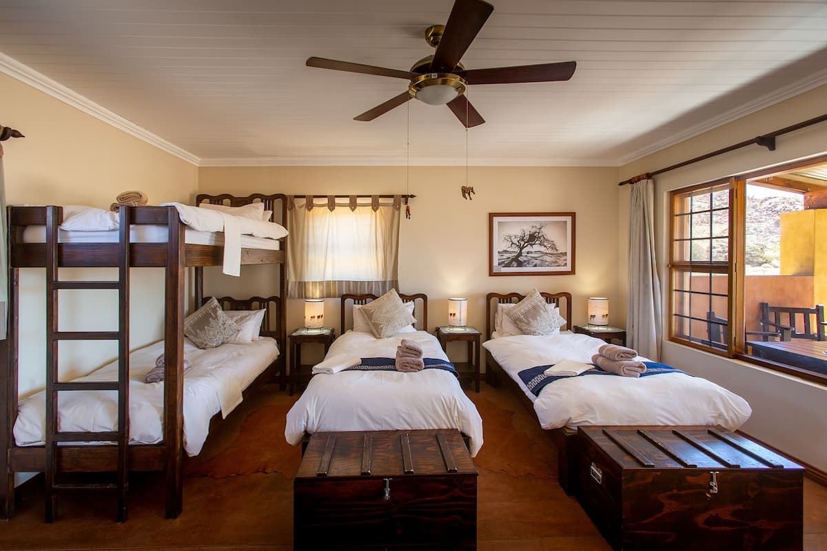 A hotel room with bunk beds, a ceiling fan, bedside lamps, a window with curtains, and a framed picture on the wall.
