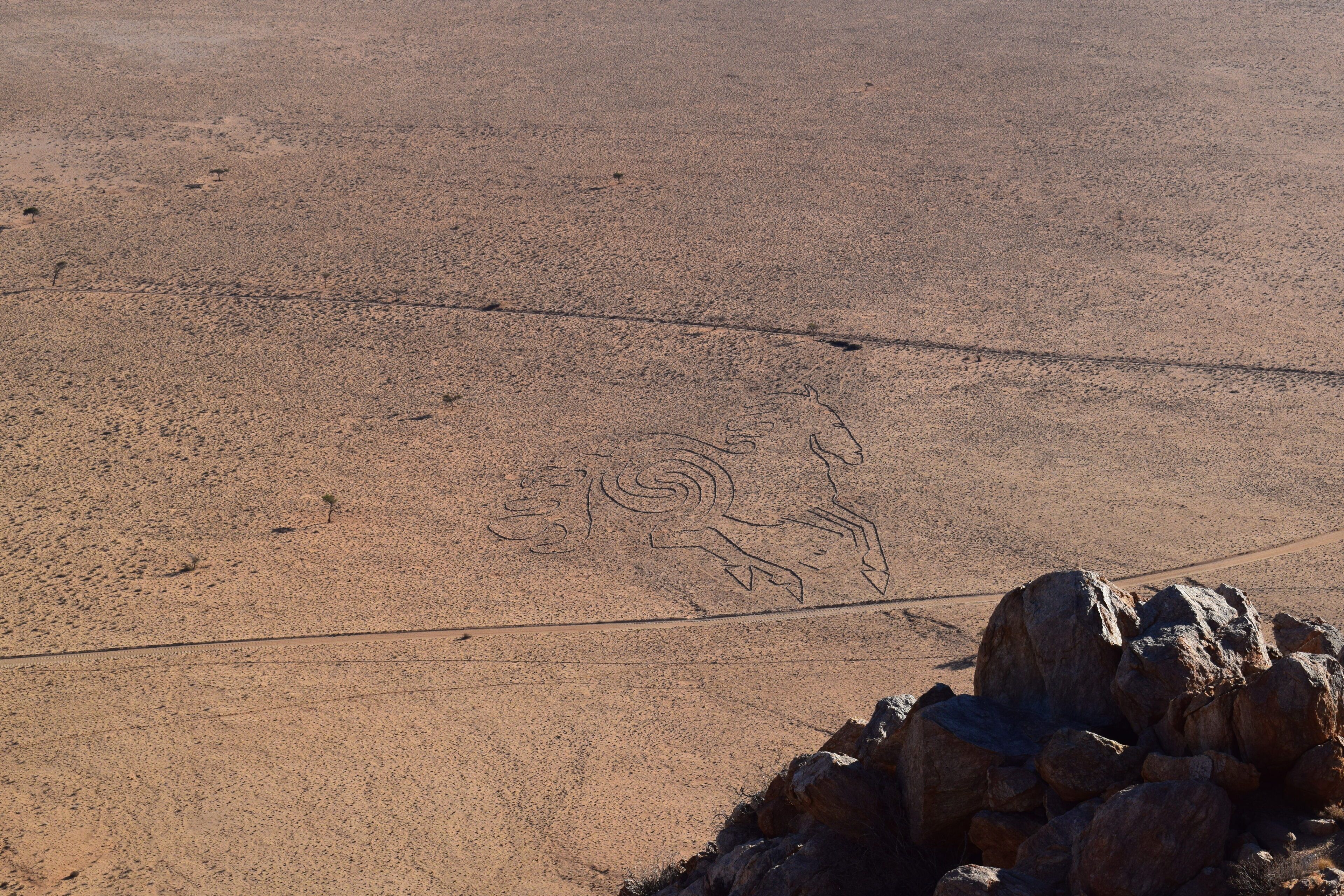 A desert landscape with a large rock formation in the foreground and a faint animal track in the sand.