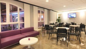 A modern lounge area with a purple sofa, round tables, and black chairs. - Bilbaino (Benidorm)