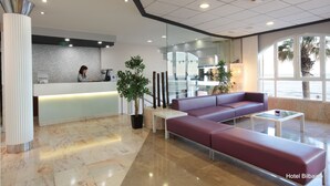 A modern hotel lobby with a reception desk, seating area, and large windows. - Bilbaino (Benidorm)