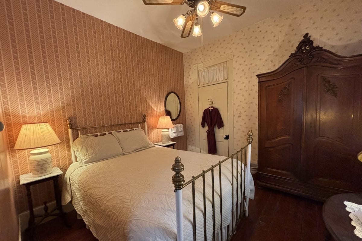 Un dormitorio con cama, mesita de noche, lámpara, armario y espejo.