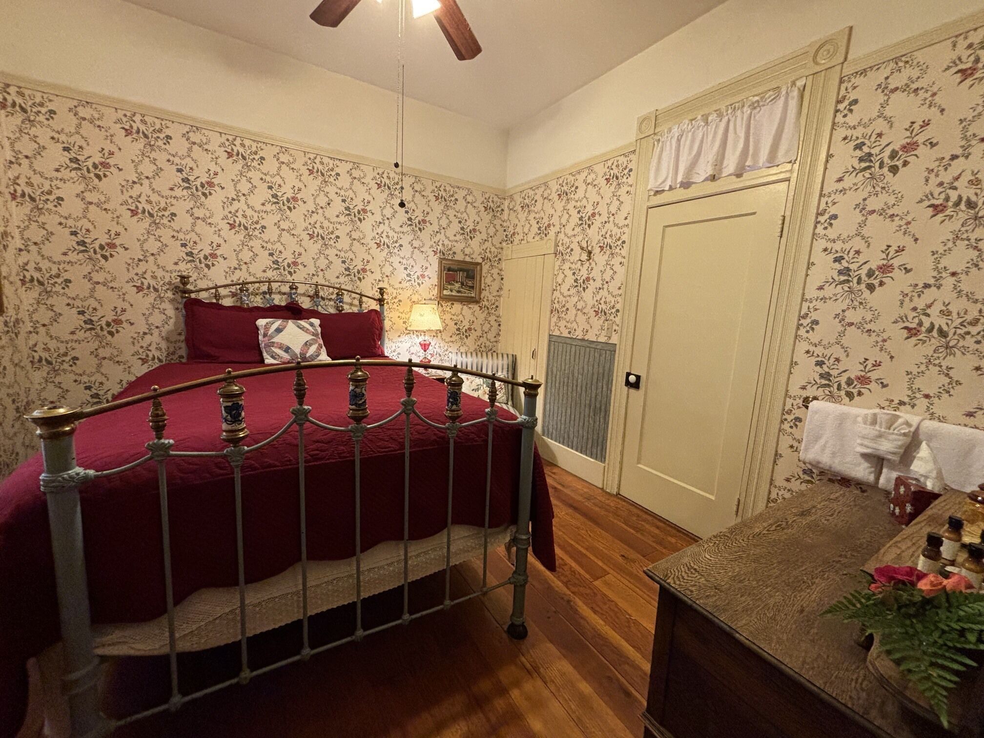 Een slaapkamer met een bed, een dressoir, een radiator en bloemenbehang.