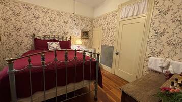 Een slaapkamer met een bed, een dressoir, een radiator en bloemenbehang.