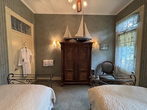 Une chambre avec deux lits, une armoire en bois, une chaise et une fenêtre ornée de rideaux à motifs.