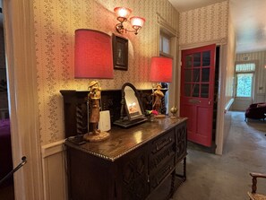 A wooden dresser with a mirror, two wall-mounted lamps, and a red door in a room with patterned wallpaper.