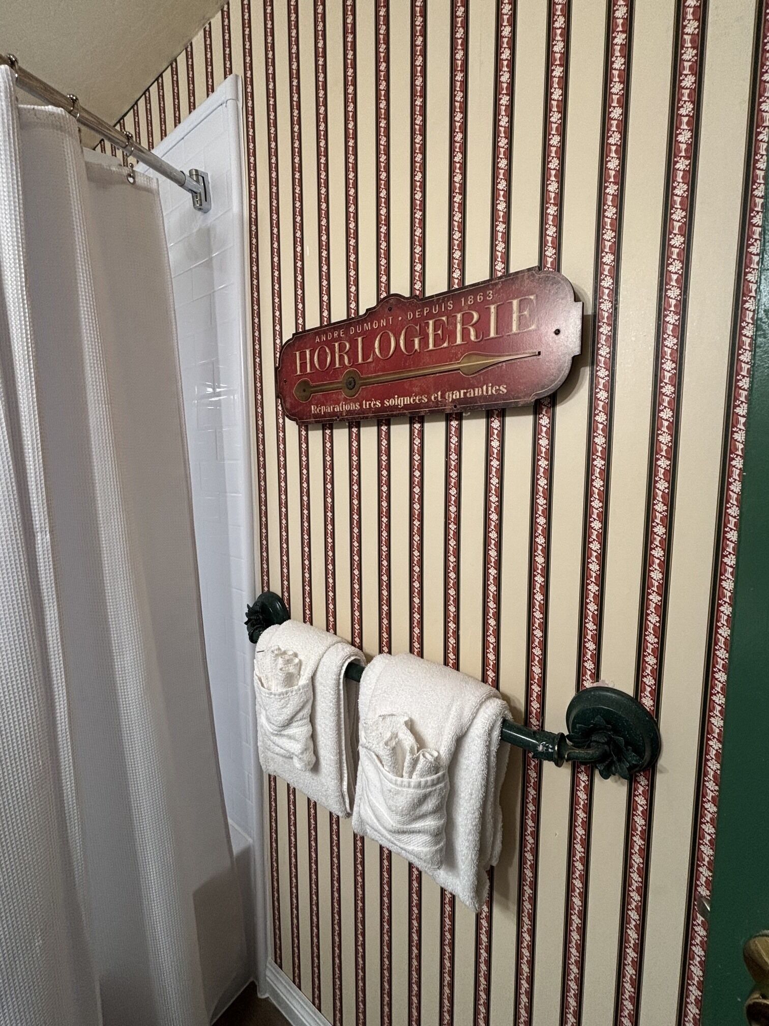 Ein Badezimmer mit gestreifter Tapete, einer Duschvorhangs und einem Handtuchhalter mit zwei Handtüchern.