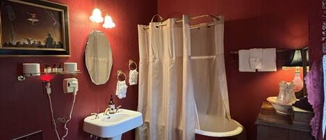 Un baño con suelo de madera, un lavabo blanco, un inodoro, una cortina de ducha y un espejo.