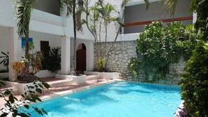 A swimming pool with a stone wall and palm trees. - Hotel Plaza Carrillo's (Cancun)