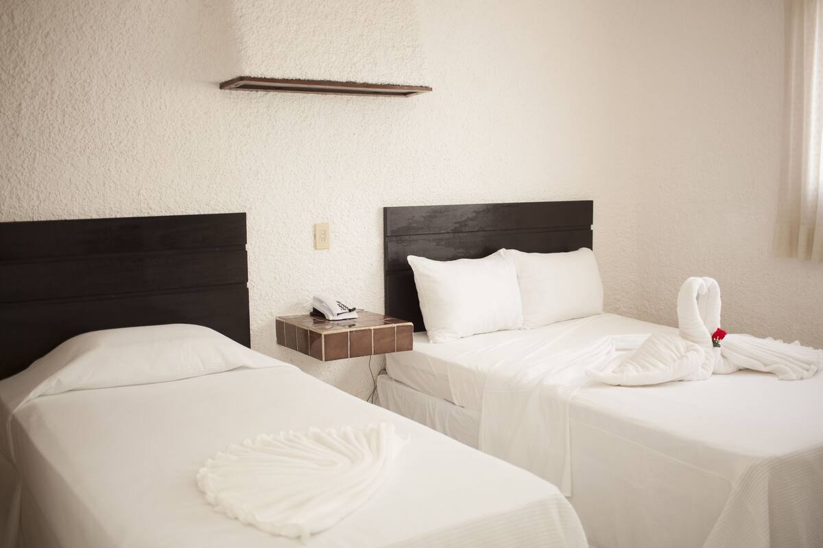 Two single beds with white linens, a wooden nightstand with a phone, and a towel on the right bed.
