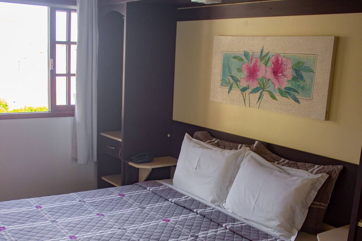 A neatly made bed with a quilted cover, a bedside table, a nightstand, and a wall-mounted painting.