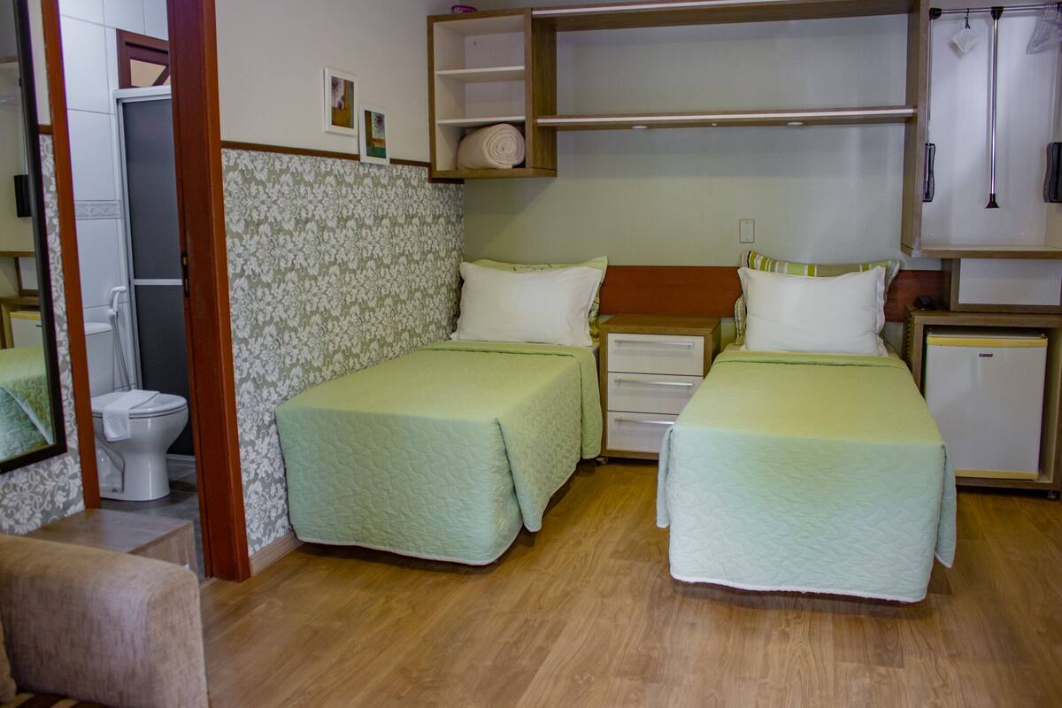 A room with two beds, a small cabinet, a toilet, and a mirror.