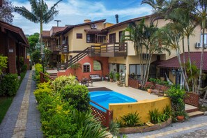 A courtyard with a swimming pool, outdoor furniture, and lush greenery. - Pousada do Atobá (Florianópolis)