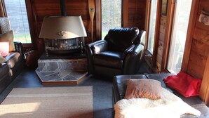 Una sala de estar acogedora con chimenea de piedra, mobiliario de cuero y vistas al exterior.