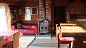 Interior acogedor de una cabaña con un sofá rojo, una mesa de madera y una chimenea de ladrillo.