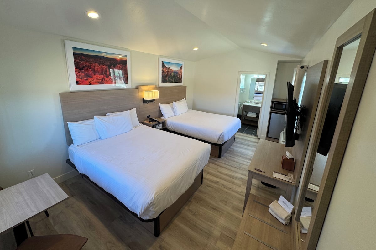 A hotel room with two beds, a desk, a TV, and artwork on the walls.