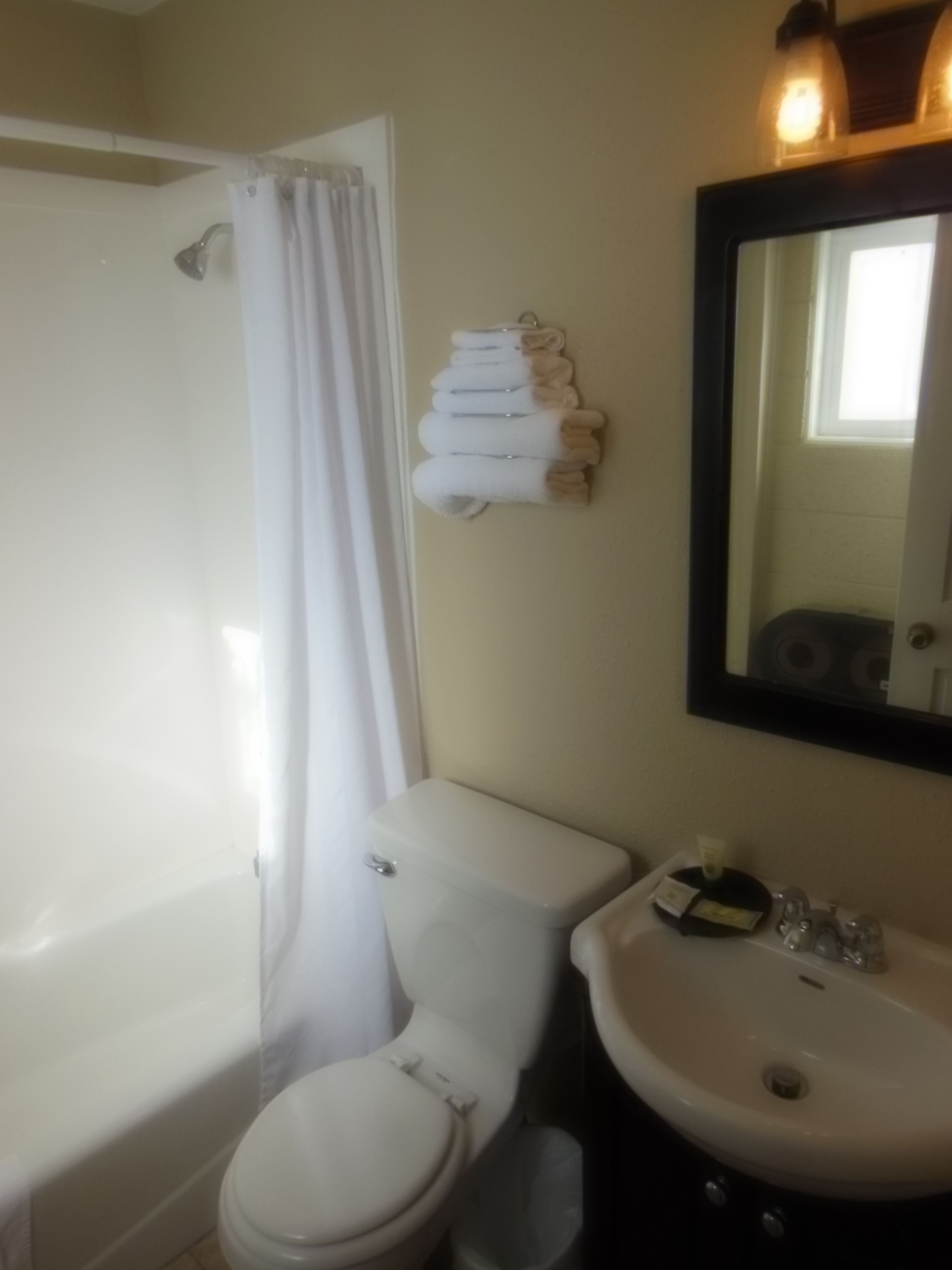 A bathroom with a toilet, sink, and shower. There are towels hanging on the wall.