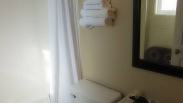 A bathroom with a toilet, sink, and shower. There are towels hanging on the wall.