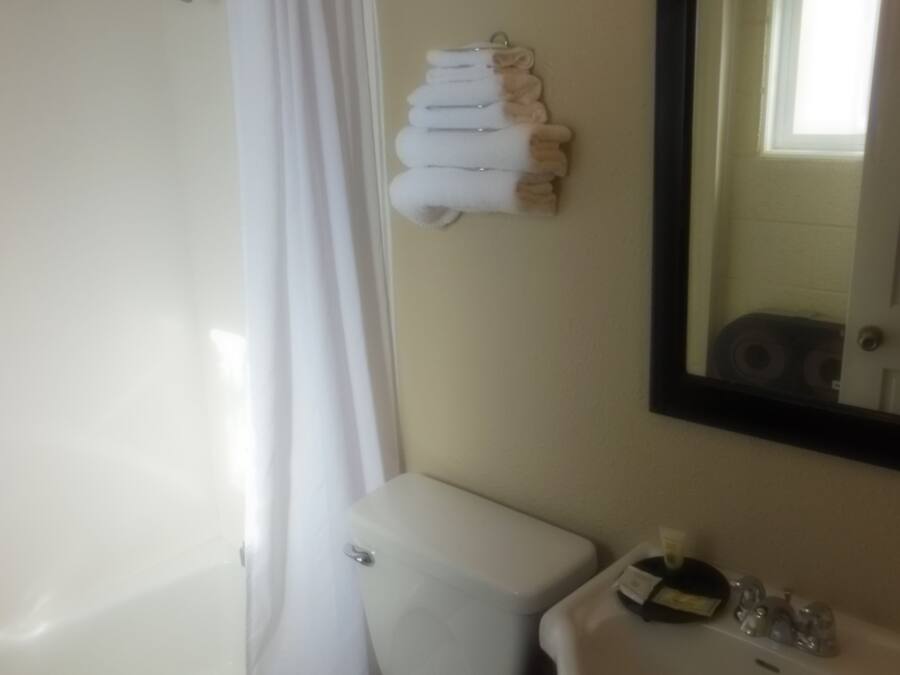 A bathroom with a toilet, sink, and shower. There are towels hanging on the wall.