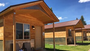 A wooden cabin with a porch, a window, and a door. There are two chairs on the porch.