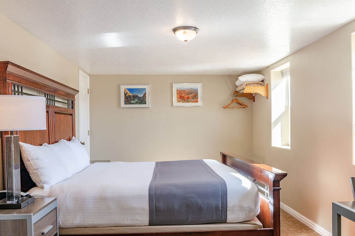 A neatly made bed with a headboard, a bedside table with a lamp, and two framed pictures on the wall.