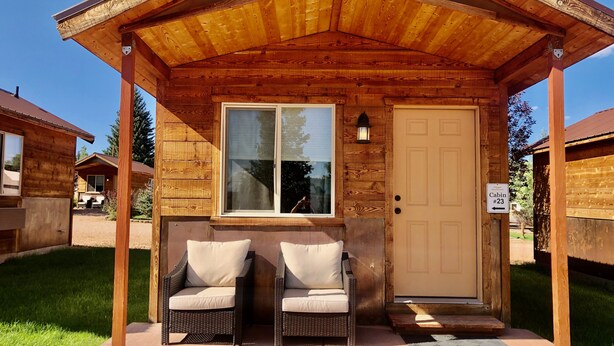 A wooden cabin with a porch, two wicker chairs, a door, and a window. - Mountain Ridge Cabins and Lodging (Hatch)