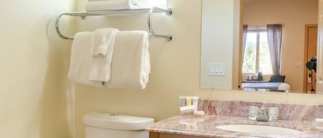 A bathroom with a toilet, sink, and mirror. There are towels on a rack and a window above the toilet.