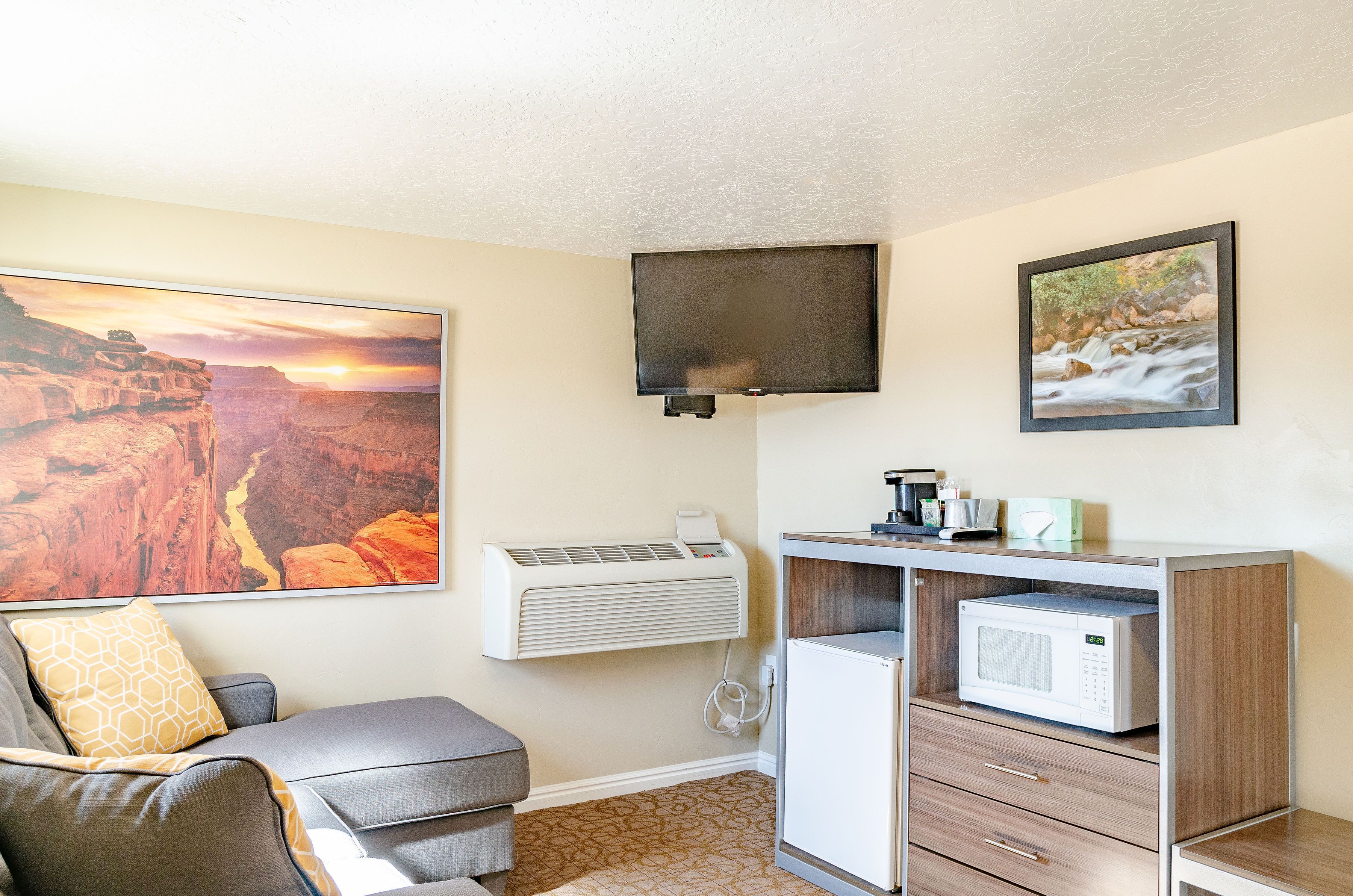 A room with a sofa, a mounted TV, a microwave, and a refrigerator.