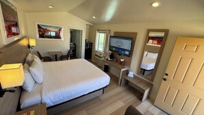 A hotel room with a large bed, a desk with a computer, a TV, and a door.