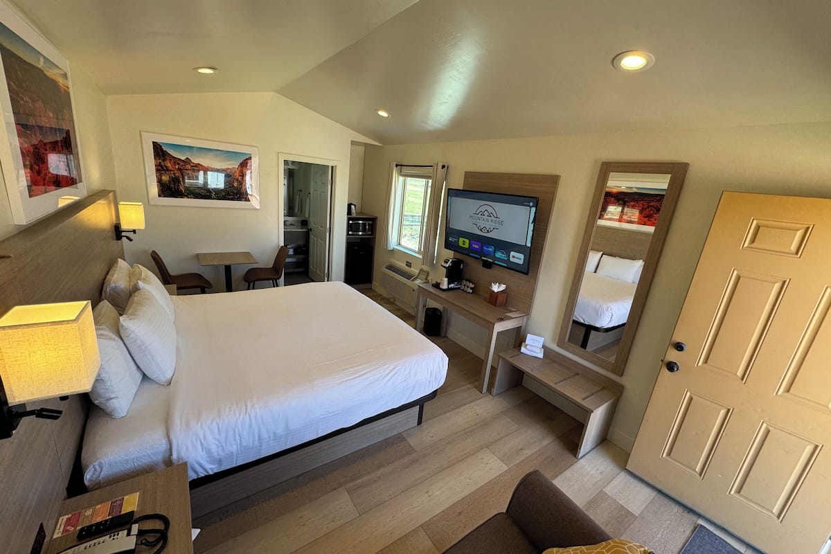 A hotel room with a large bed, a desk with a computer, a TV, and a door.