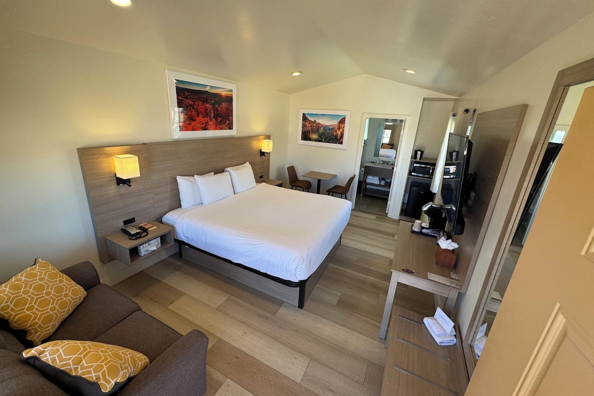 A hotel room with a large bed, a sofa, a desk, and a kitchenette.