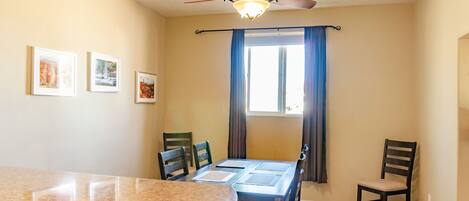 A dining area with a round table, chairs, a ceiling fan, and a window with curtains.
