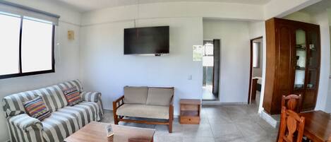 A living room with a sofa, armchair, coffee table, TV, and dining set.