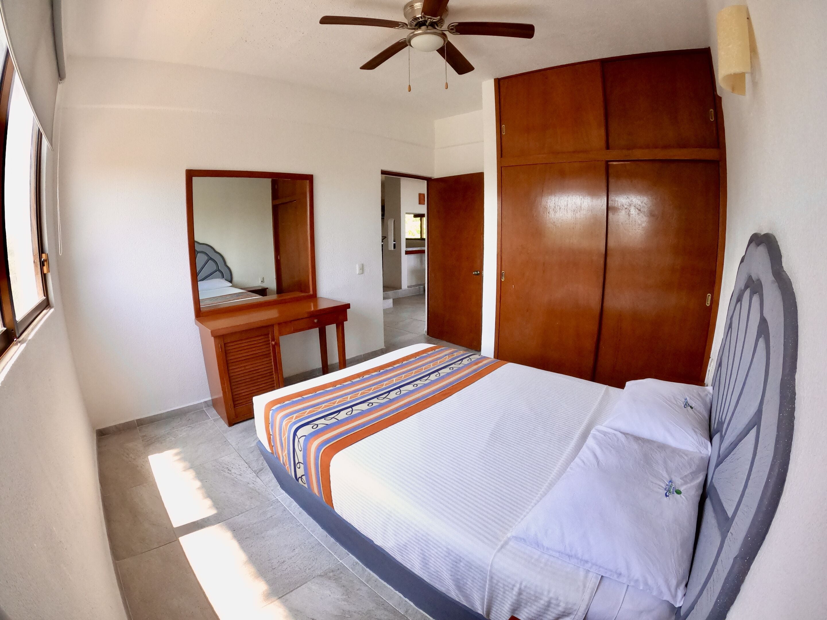 Una camera da letto con un letto, un'armadio in legno, una scrivania e una ventola a soffitto.