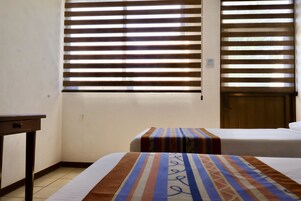 Habitación de hotel con dos camas, una mesita y una ventana con persianas.