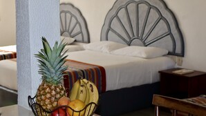 Et hotelværelse med en seng, et natbord og en frugtkurv med ananas, bananer og appelsiner.