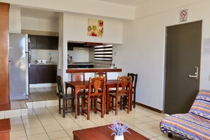 A compact hotel room with a kitchenette, a dining area with wooden furniture, and a bed with patterned bedding. - Quinta Carrizalillo (Puerto Escondido)