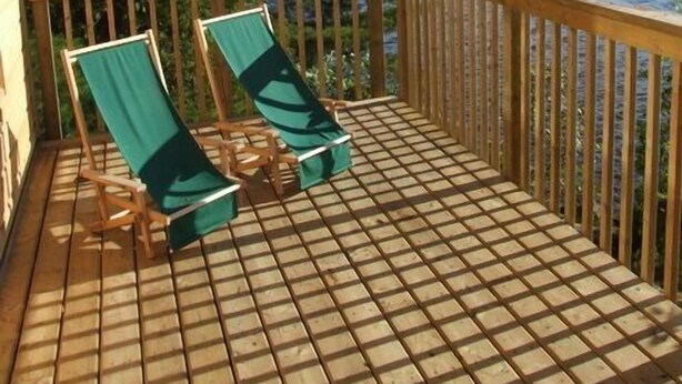 Een houten terras met twee groene lounge fauteuils gericht op een meer.