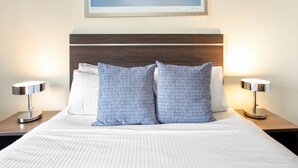 Una cama bien hecha con colcha a rayas, dos almohadas estampadas y dos lámparas de noche.
