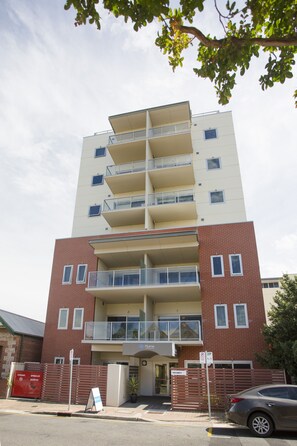 Un edificio de varios pisos con balcones, entrada protegida por un portón y un cartel que indica disponibilidad.