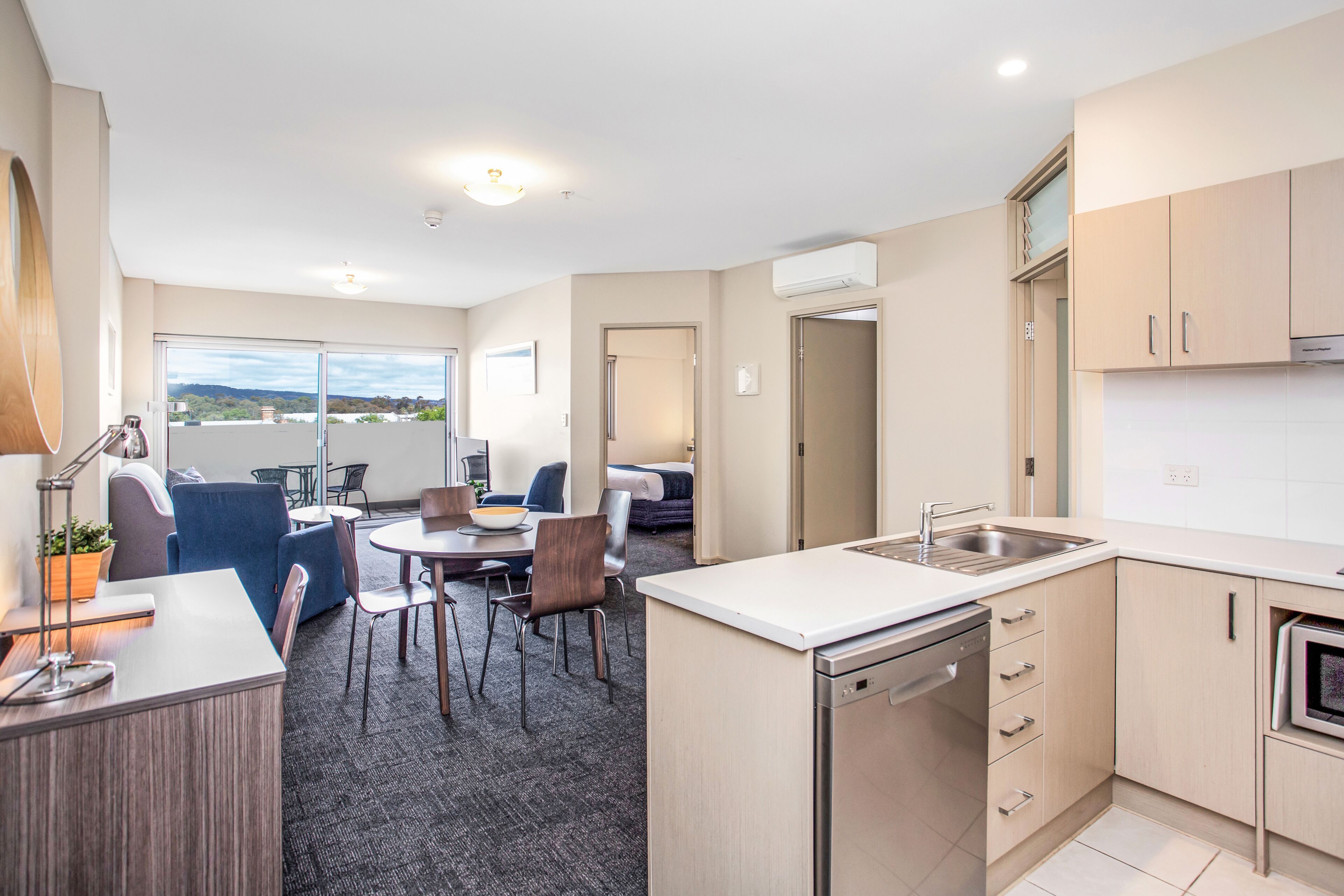 A modern kitchen with a dishwasher, a dining area with a table and chairs, and a view of the outdoors.