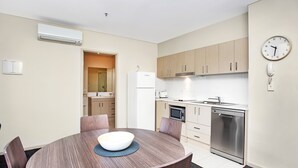 Cocina moderna con armarios de madera, horno empotrado, microondas y lavavajillas. Hay una mesa redonda con sillas y un tazón encima.