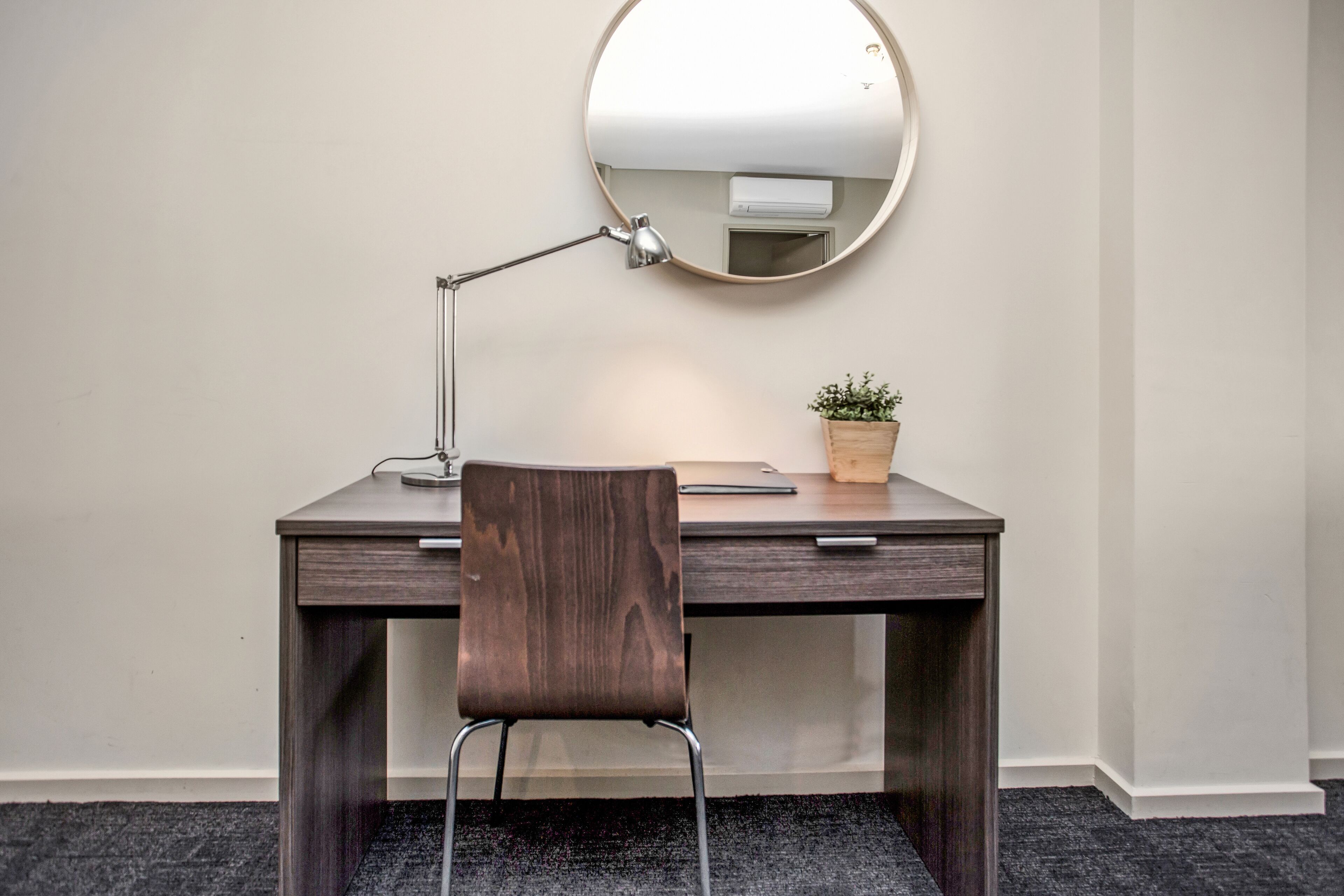 Een bureau met stoel, een ronde spiegel, een bureaulamp en een kleine plant in pot.
