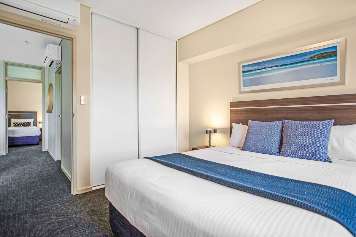 Una habitación de hotel con una cama, una mesita de noche, un cuadro y vistas a otra habitación.