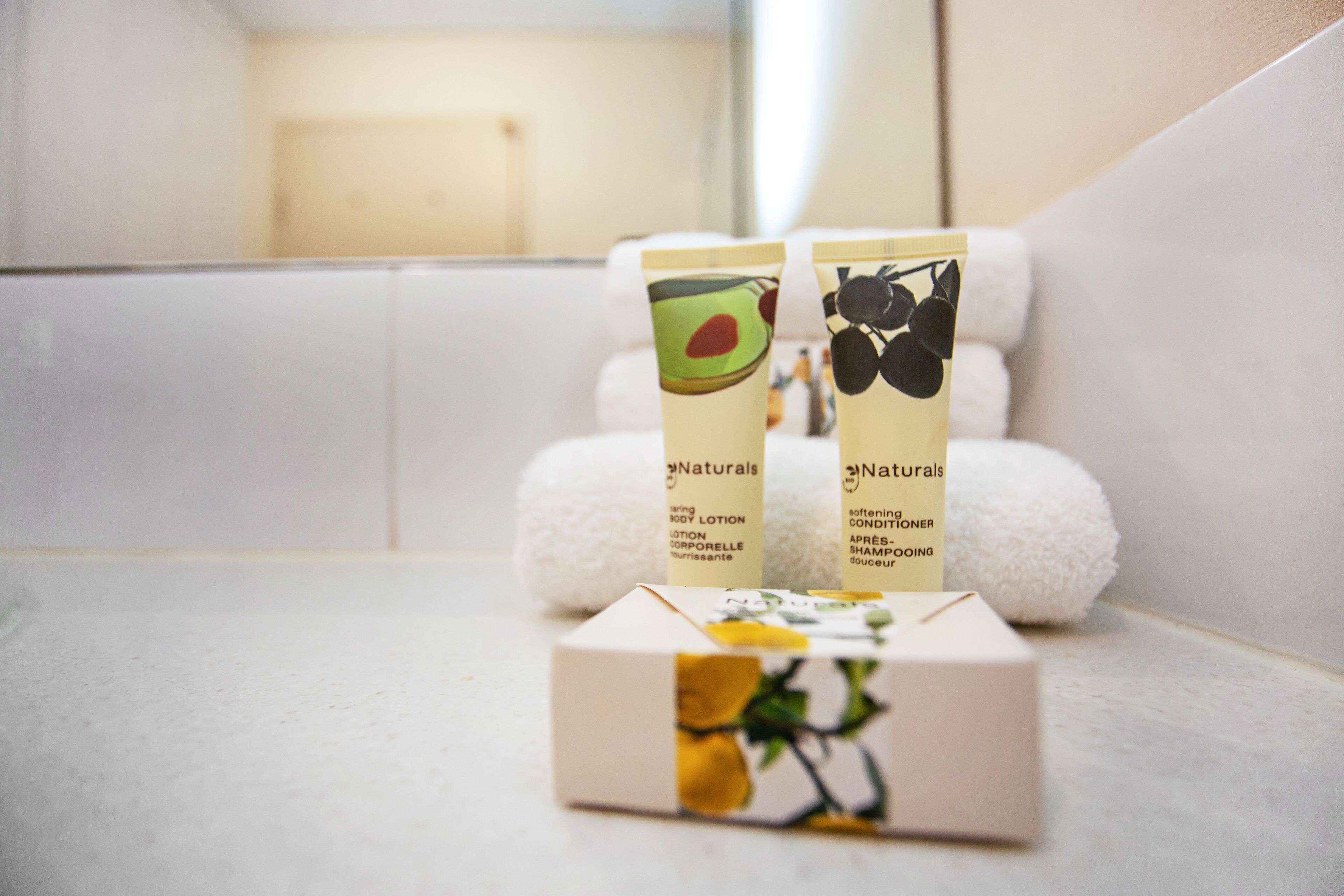 A bathroom with two bottles of Naturals body lotion and a box of Naturals shampoo.
