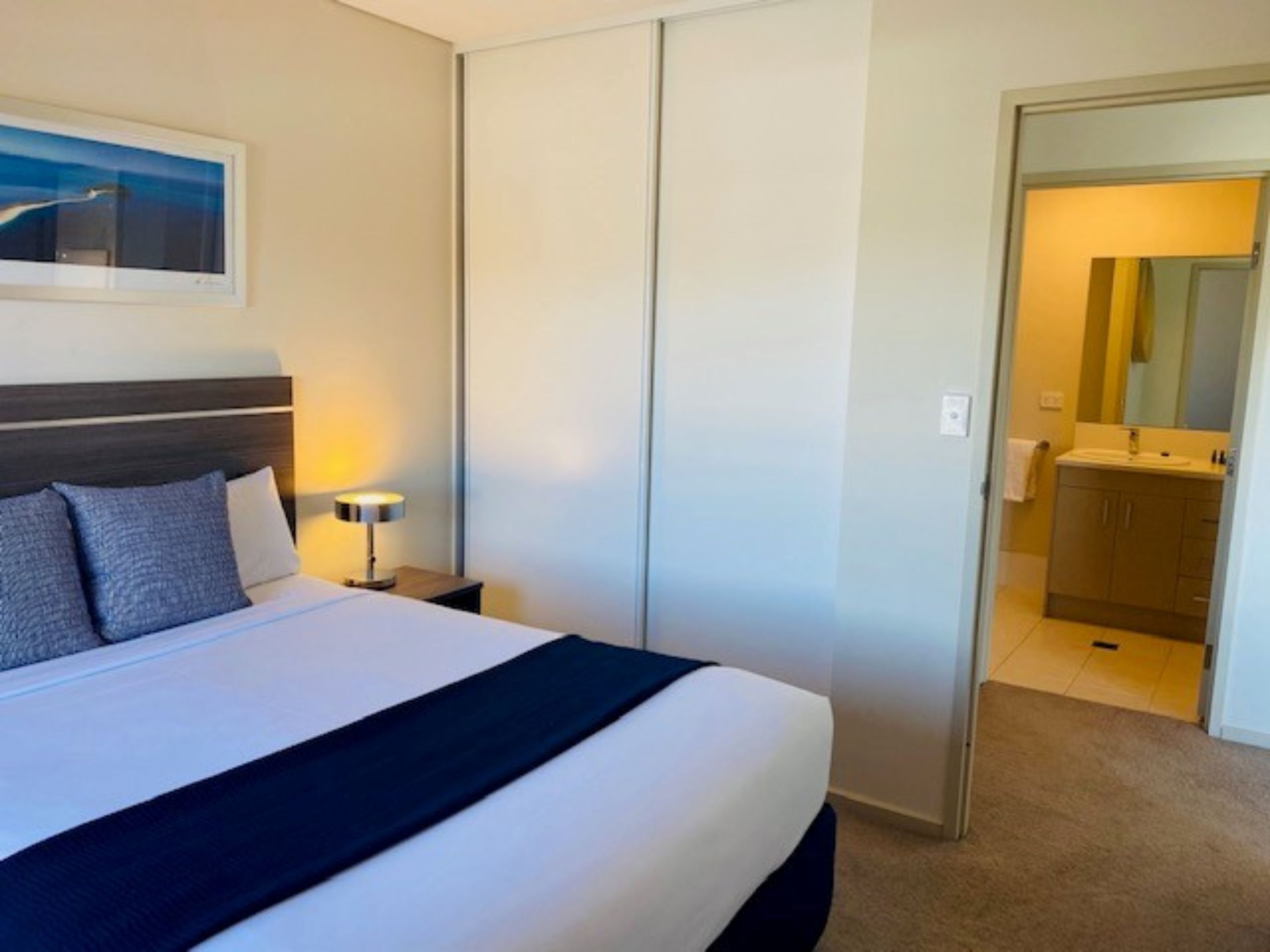 Una habitación de hotel con cama, lámpara de noche y vista al baño.